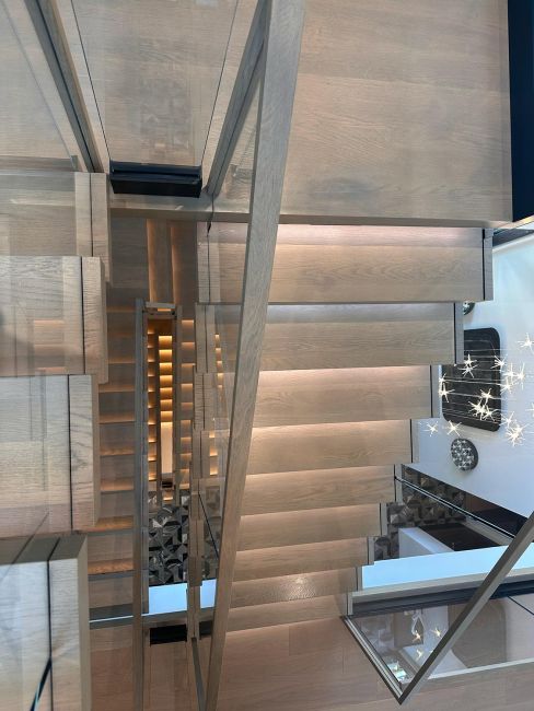 Downward look from upper landing of floating wood and glass paneled modern staircase