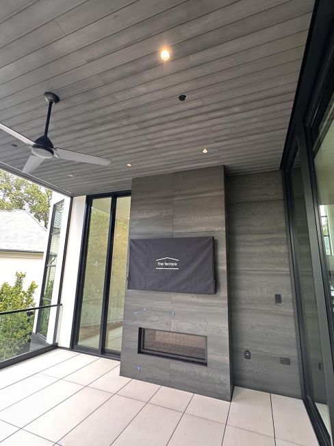 Covered modern patio with gray tiled fireplace, a ceiling fan, and covered display screen