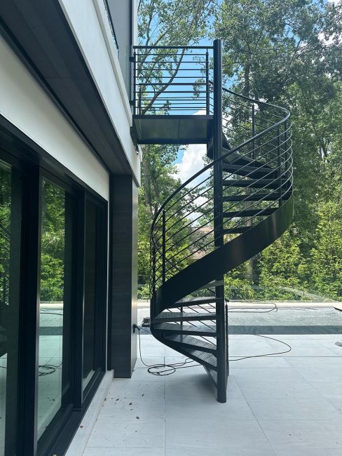 Black steel spiral staircase connecting a tiled balcony down to a lower patio