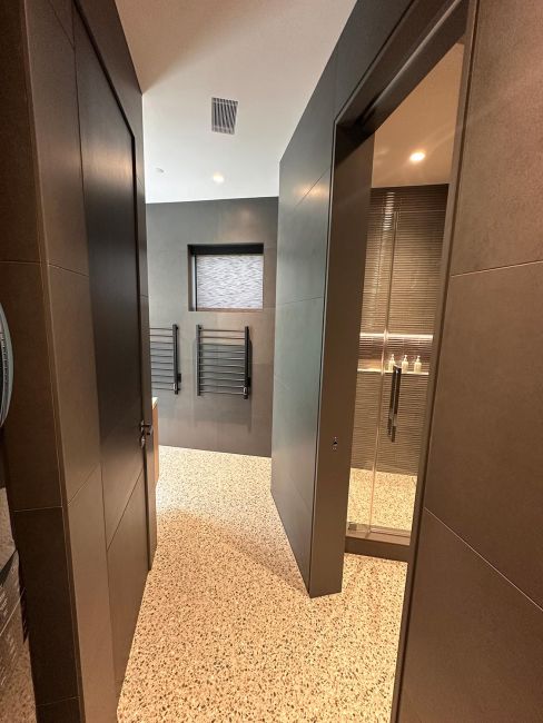 Entry hallway to modern bathroom with terrazzo stone flooring and dark slate walls