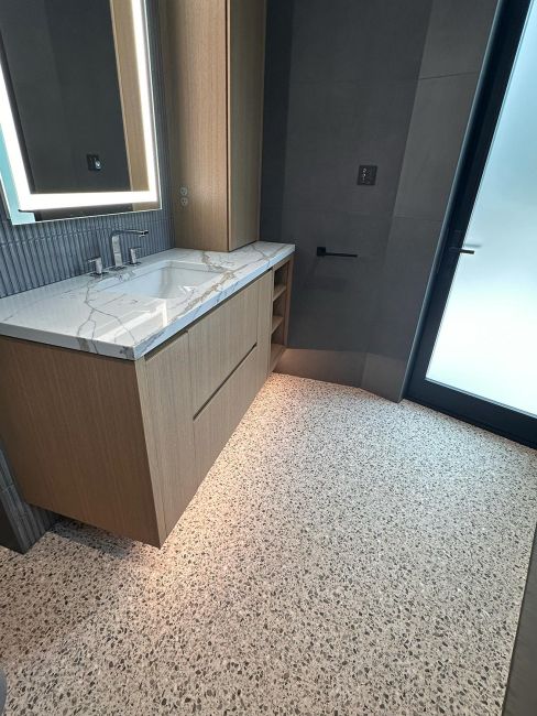 Modern bathroom vanity with light wood cabinetry, white marble counter, and illuminated mirror