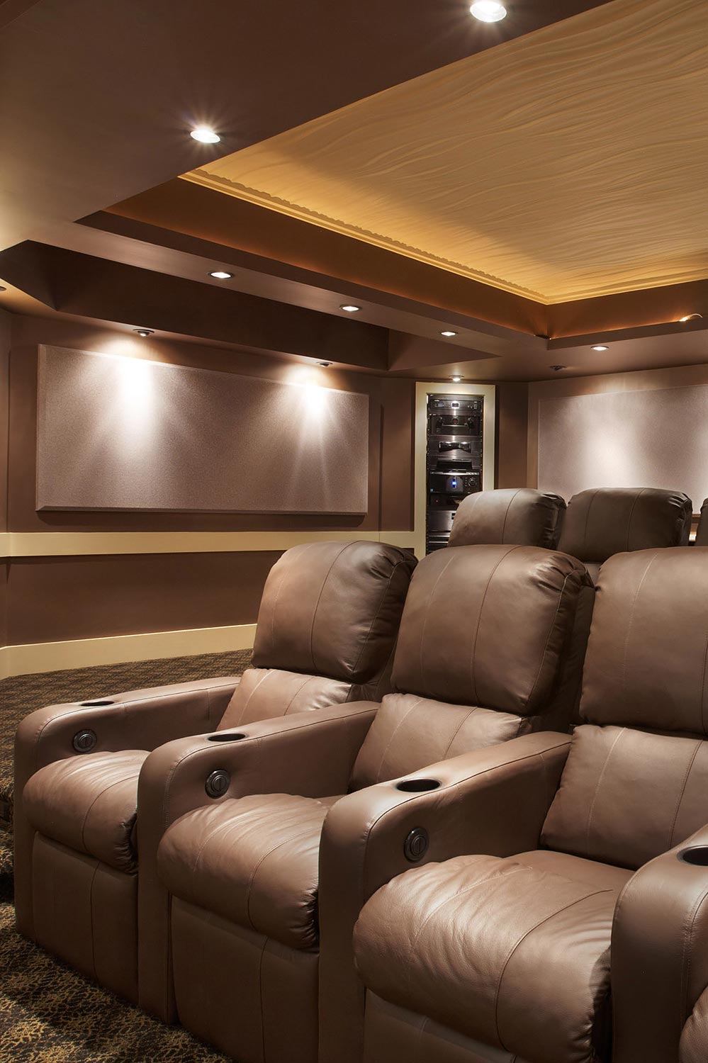 Rows of premium brown leather theater recliners underneath a warm glowing tray ceiling