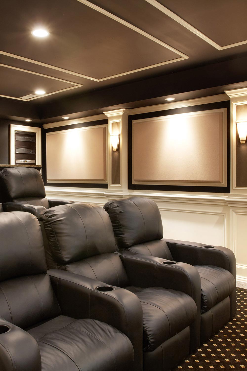 Luxury home theater with rows of black leather reclining seats and elegant wall sconces