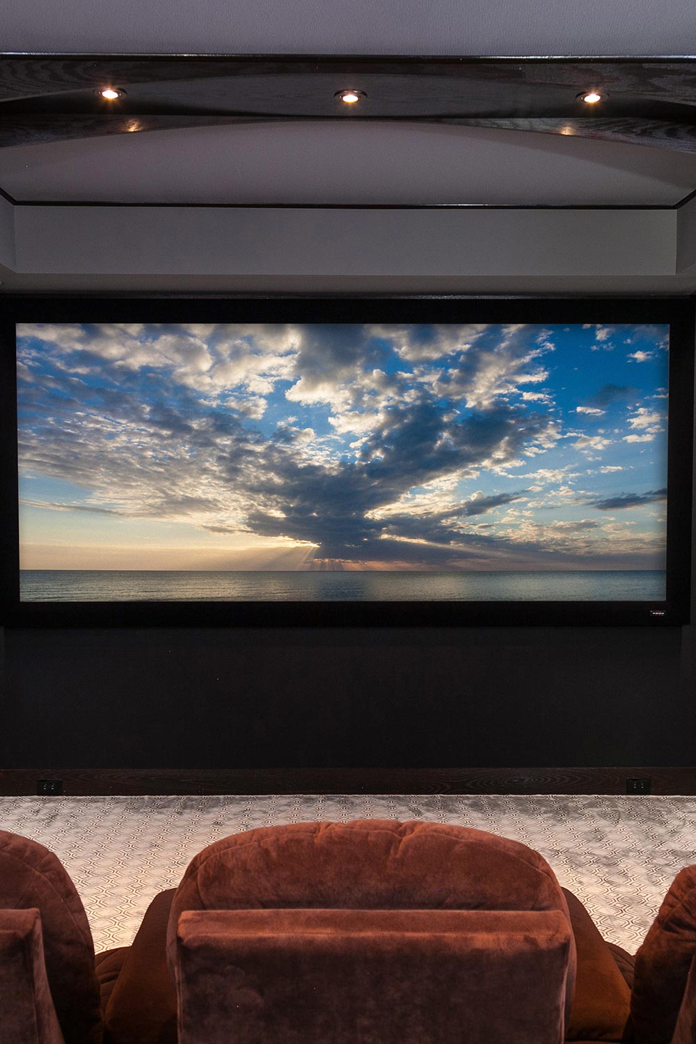 Center view of a large home theater screen displaying a sunset over the ocean
