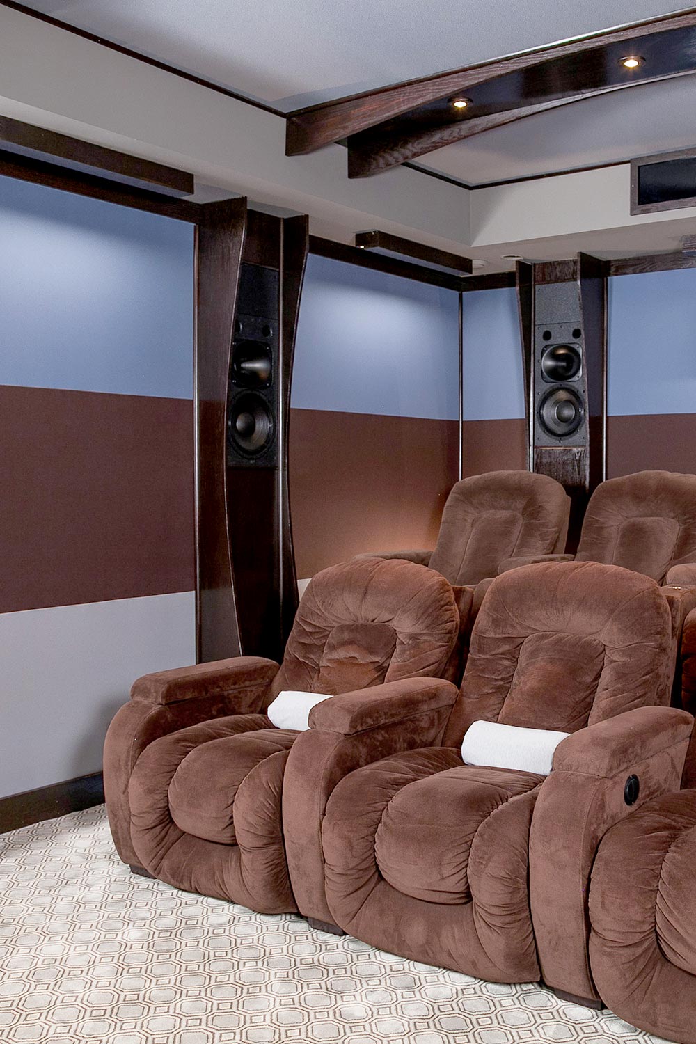 High-end home cinema speakers built into wood pillars behind plush brown suede recliners