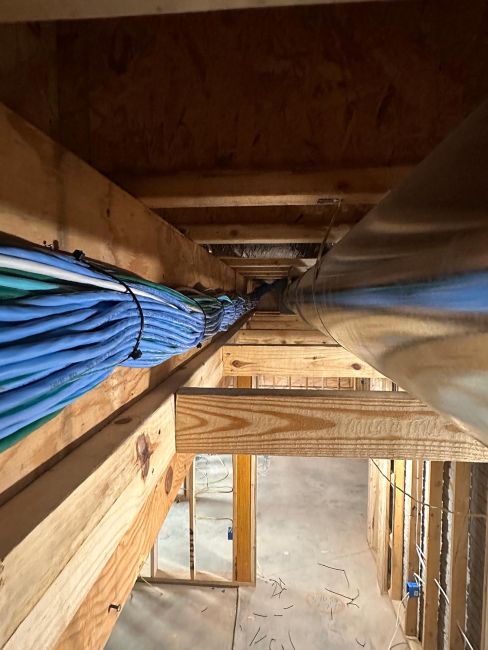 View between wooden ceiling joists showing a thick bundle of blue wires running along a duct
