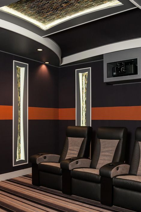 Contemporary media room with two-tone leather recliners, dark walls, and orange accents