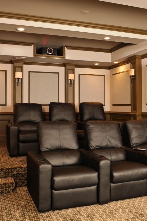 Multi-tiered home theater seating with black leather chairs and integrated ceiling projector