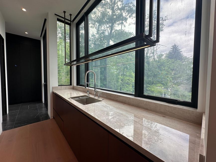 Marble kitchen countertop with metallic sink and long window overlooking green trees