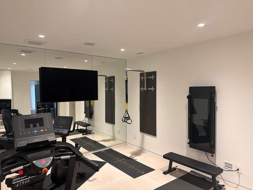 Interior home fitness center room with treadmill, gym bench, and full wall mirror