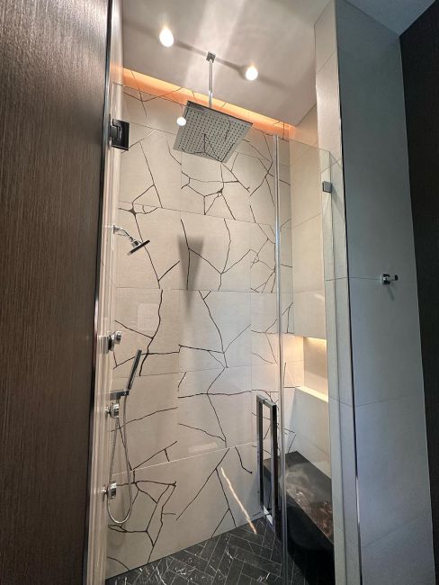 Walk-in shower with large white tiles featuring a custom black cracked pattern design