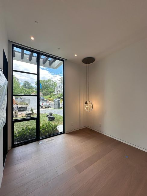 Empty room featuring light hardwood floors, large window, and minimalist pendant light