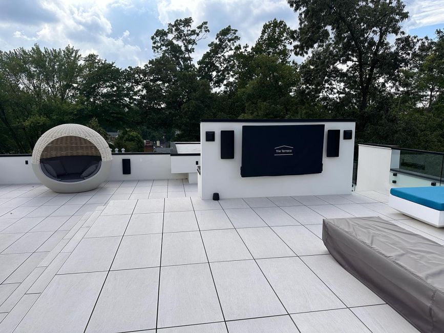 Tiled rooftop lounge area with modern white wicker shade daybed and covered display screen