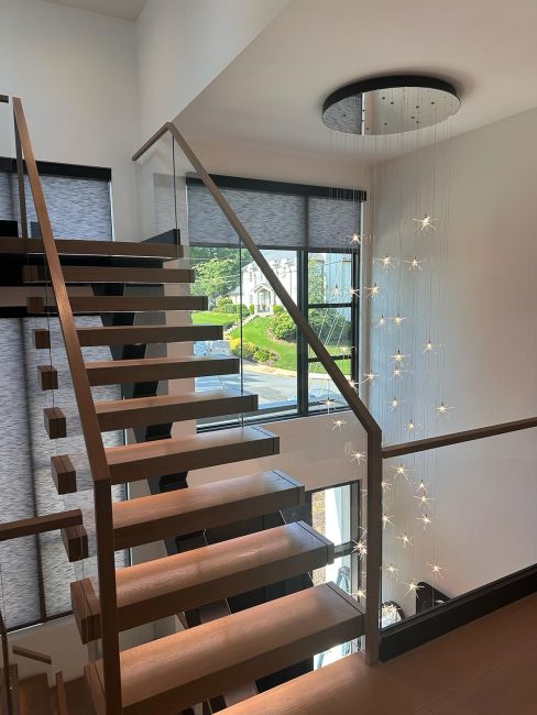 Floating wood step staircase positioned beside massive multi-story glass window panes