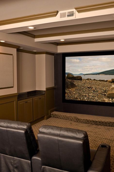 View of a home cinema screen showing a rocky shoreline in front of black leather seating
