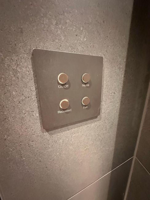 Dark gray wall keypad with four metallic buttons for on, off, niche, recessed, and fan
