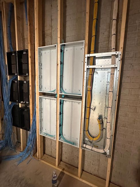 Unfinished utility area showing wood wall framing with metal enclosures and blue cables