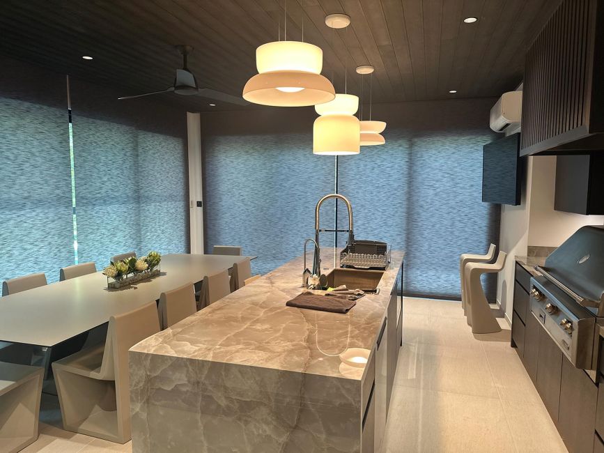 Long kitchen island with polished marble countertop and designer white pendant lights