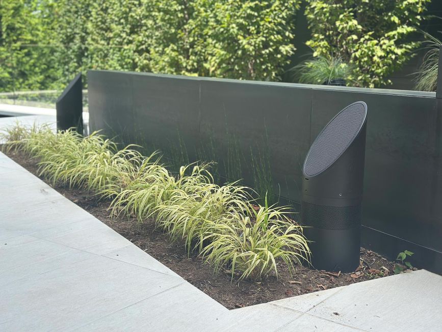 Black circular architectural outdoor speaker installed inside a garden landscape bed