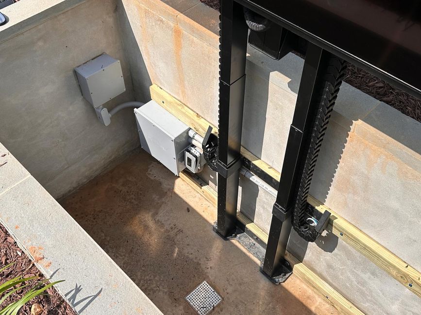 Interior view of the outdoor TV lift vault showing weather-resistant electrical boxes, conduit lines, and the black cable carrier track system.
