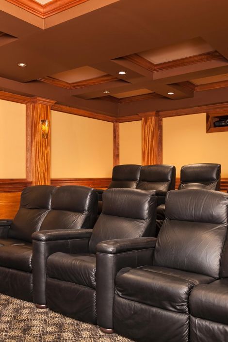 Multi-tiered home theater seating with black leather recliners and wood-trimmed ceilings