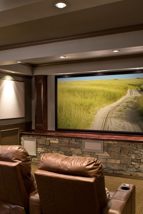 Home cinema featuring a stone accent wall beneath a large screen and brown leather seats