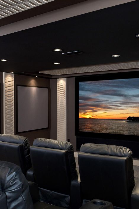 Side view of black theater recliners facing a large screen with a coastal sunset image