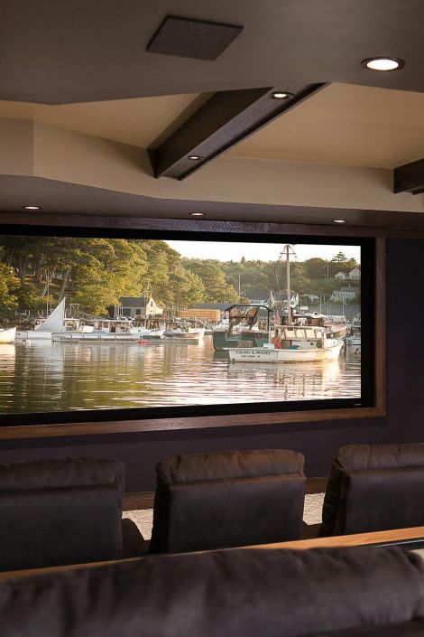 Large home theater screen displaying a harbor scene with boats behind dark recliners