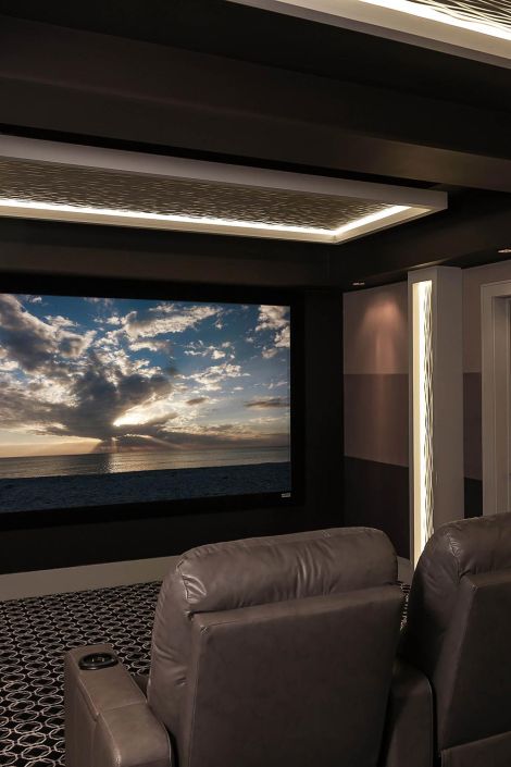 Modern media room featuring a large projection screen, gray recliners, and backlit wall panels