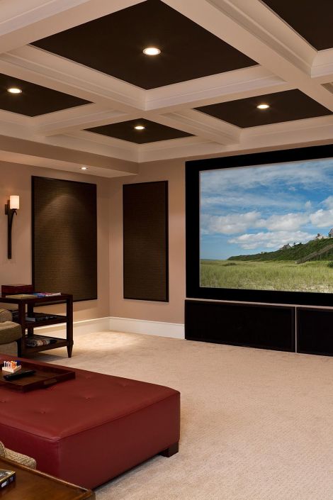 Spacious home entertainment room with a coffered ceiling, large screen, and a red ottoman