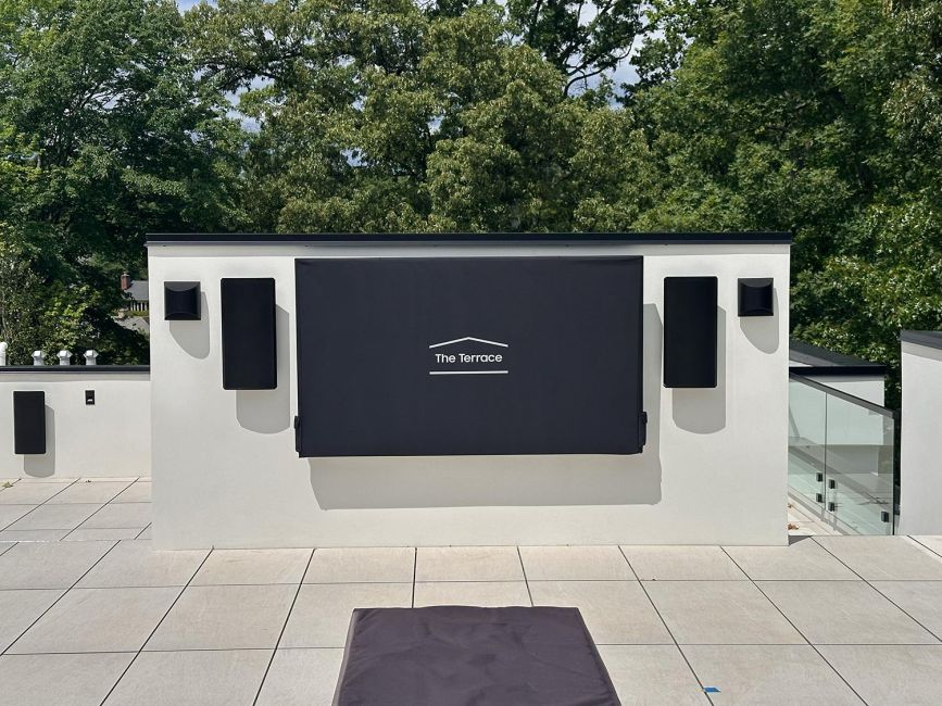 Large rooftop terrace with tiled flooring and wall-mounted television under a fabric cover