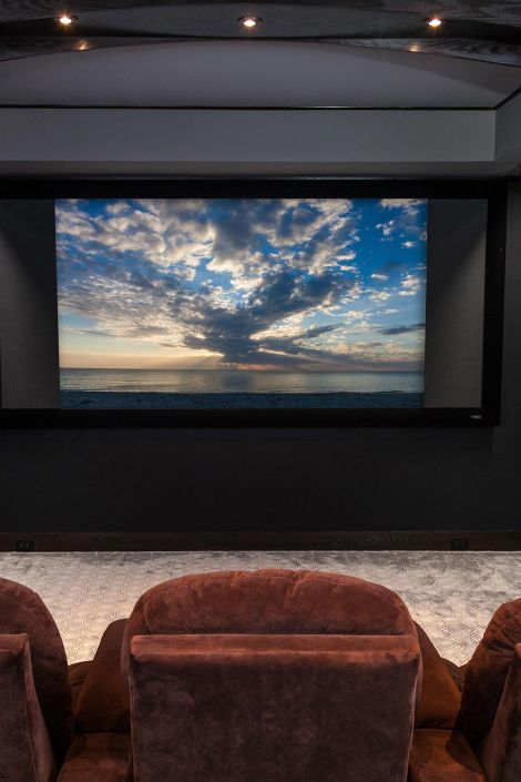 Front view of a widescreen home theater displaying a cloudy ocean sunset above brown seats
