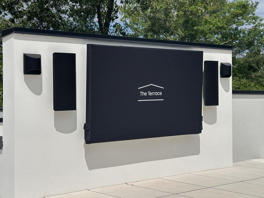 White terrace wall featuring covered outdoor television screen and black modern speakers